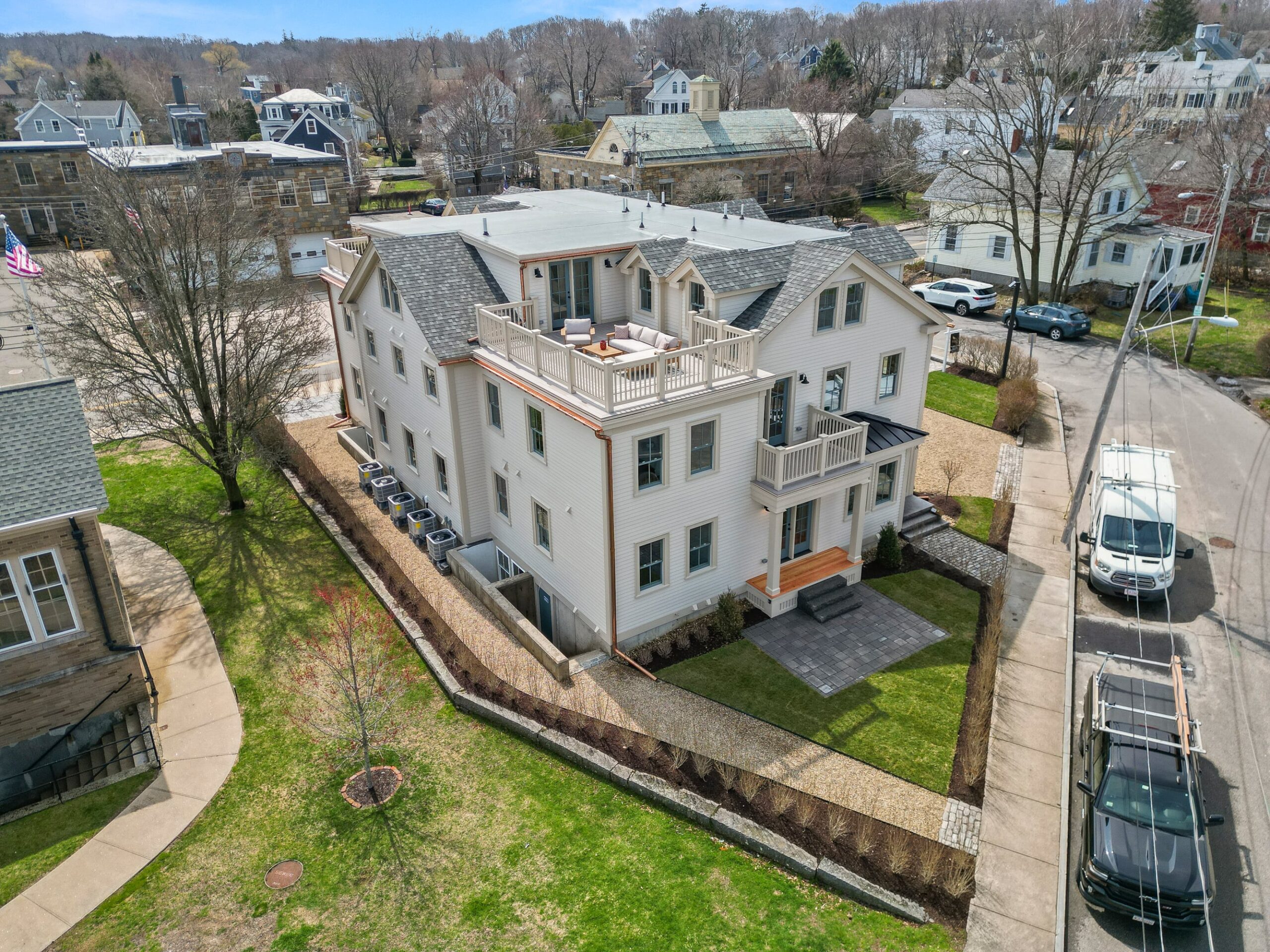 Aerial view of One Jewett Street, a multi-story white residential building with multiple balconies, surrounded by a fence and neighboring houses on a sunny day.