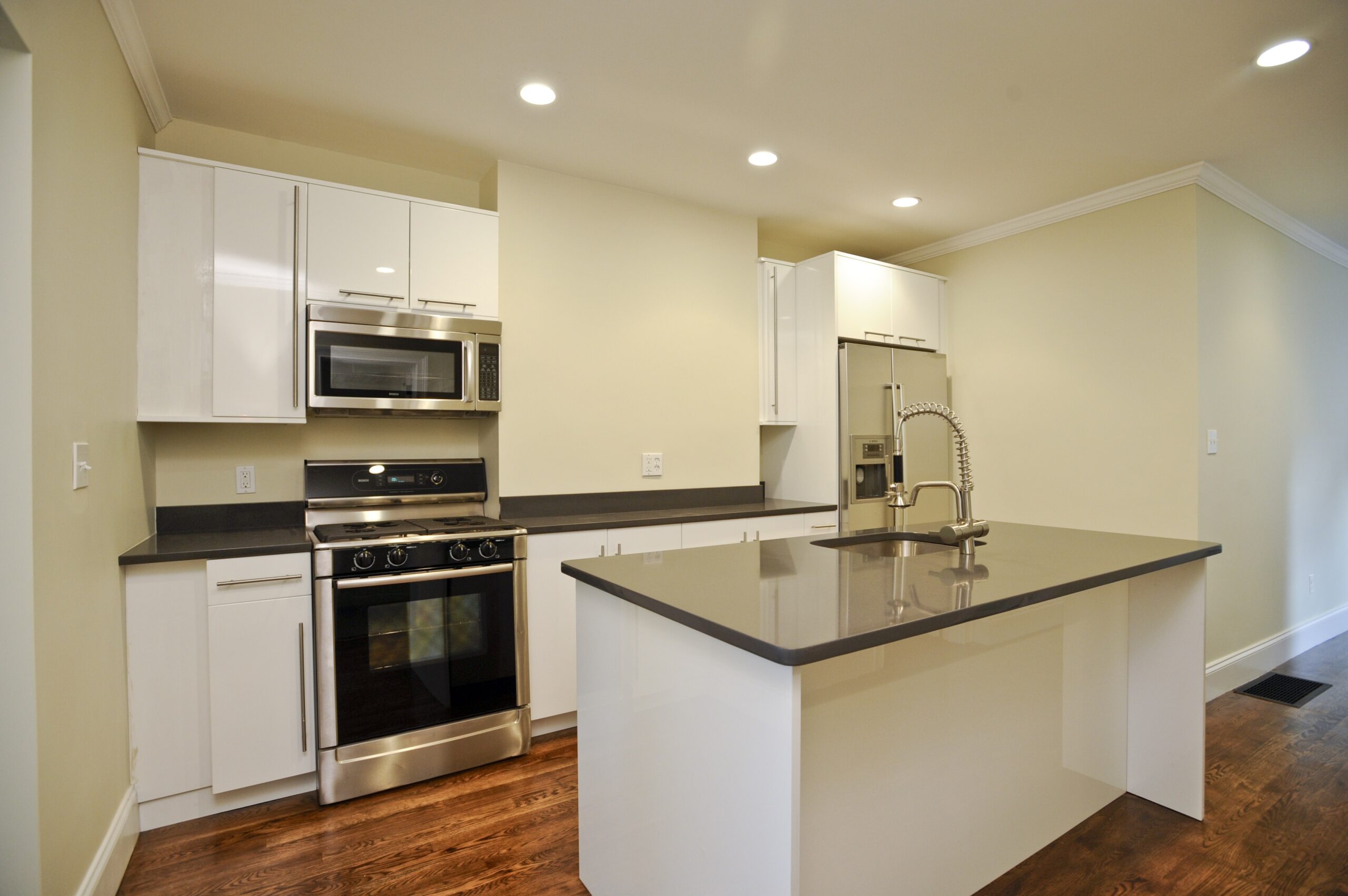 Modern kitchen on Greenview Avenue with white cabinets, stainless steel appliances, a center island with sink, recessed lighting, hardwood floors, and neutral walls.
